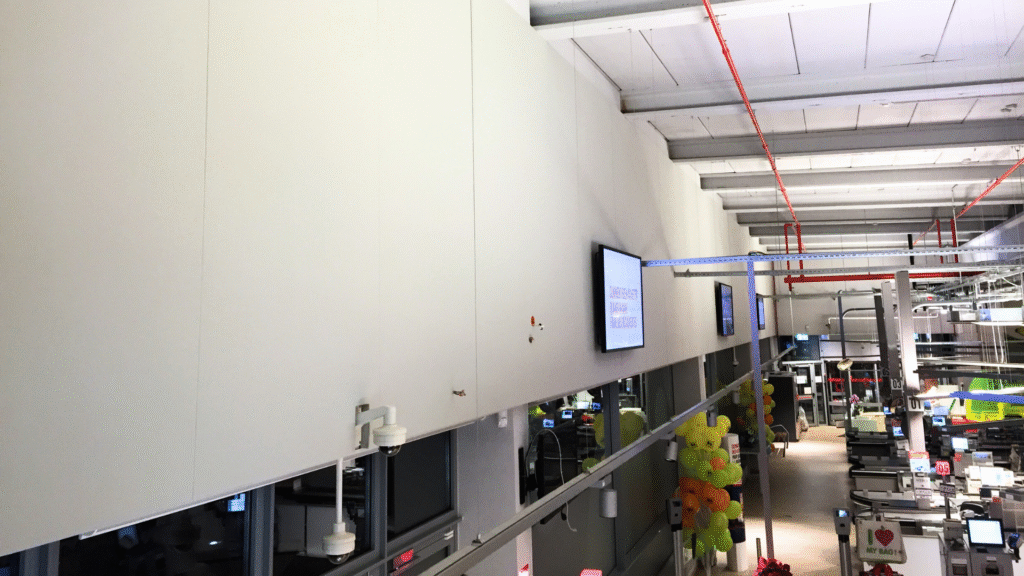 Kassazone met selfscan akoestische gestoffeerde wandpanelen en gependelde eilanden.